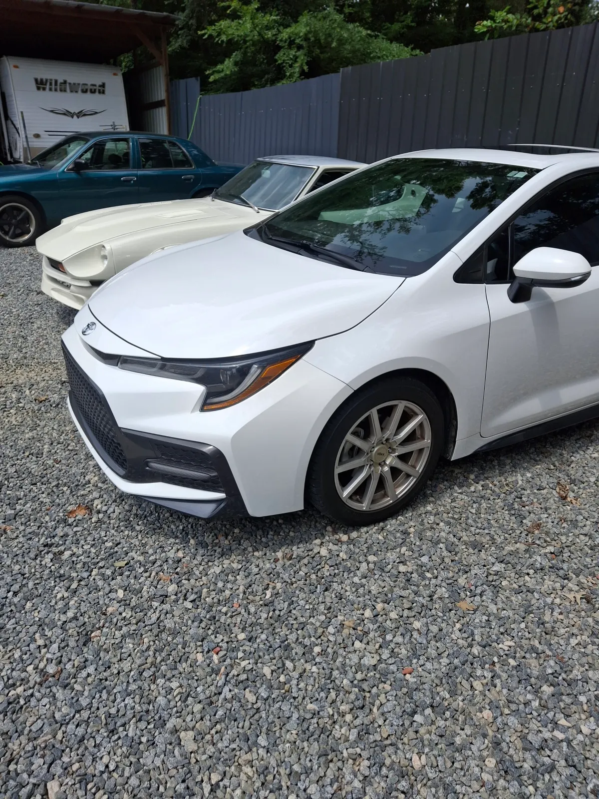 White modern sedan parked in gravel lot beside vintage coupe — The ARK Body Shop and Collision Center in Concord